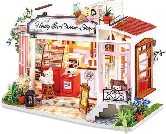 A detailed model kit of a Honey Ice Cream Shop, featuring colorful ice cream cones on the roof, charming outdoor plants, and a cozy interior with a counter, decorations, and a cute bear figure. The shop showcases intricate design elements, inviting decor, and a bright, cheerful aesthetic, perfect for DIY enthusiasts.