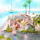 A detailed model kit of a Honey Ice Cream Shop featuring pastel colors, two cute characters in aprons, and a charming, scenic background with palm trees and a seaside view. The kit includes intricately designed elements like an outdoor seating area and decorative plants, showcasing a whimsical, inviting ice cream shop atmosphere.