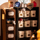 A whimsical display from Kiki's Magic Emporium by Robotime. The image showcases a shelf filled with neatly labeled boxes, containing magical items like 'Calming Draught,' 'Felix Felicis,' and 'Poltergeist Potion.' A dark cabinet holds additional boxes and items, while colorful bottles and scrolls add to the enchanting atmosphere.