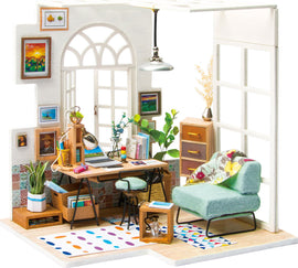 A beautifully detailed DIY miniature house model kit featuring a cozy workspace scene. It includes a desk with a desk lamp, bookshelves, a comfortable green chair, houseplants, and colorful wall art. The interior is designed with warm colors, patterned rugs, and stylish furniture, perfect for craft enthusiasts.