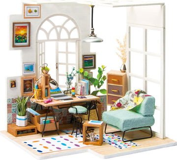 A beautifully detailed DIY miniature house model kit featuring a cozy workspace scene. It includes a desk with a desk lamp, bookshelves, a comfortable green chair, houseplants, and colorful wall art. The interior is designed with warm colors, patterned rugs, and stylish furniture, perfect for craft enthusiasts.