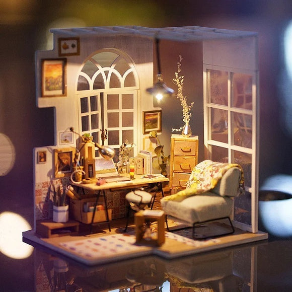 The SOHO Time DIY Miniature House Model Kit by Robotime features a beautifully detailed miniature room with a wooden desk, vintage-style chair, decorative prints on the walls, and a cozy armchair. The scene is illuminated by a stylish lamp, creating a warm atmosphere.