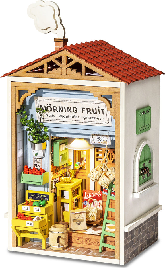 A beautifully detailed model kit of a quaint fruit store titled 'Morning Fruit'. The kit features a charming storefront with signs for fruits, vegetables, and groceries, showcasing intricate wooden elements, bright colors, and miniature decor like potted plants, baskets, and a welcoming sign. Smoke billows from a chimney, adding a whimsical touch to this DIY project.