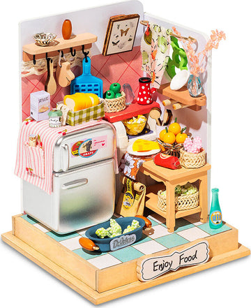 The Taste Life Kitchen Model Kit by Robotime features a beautifully detailed miniature kitchen setup. It includes a fridge adorned with labels, colorful fruits on a wooden table, utensils hanging on the wall, a cozy design with floral accents, and various kitchenware, all arranged neatly to create a lifelike culinary environment perfect for DIY enthusiasts.