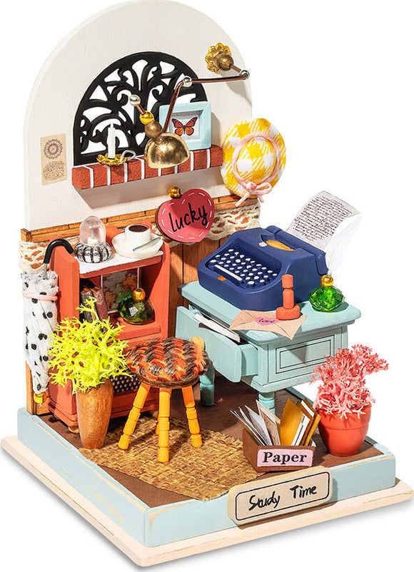 A detailed model kit by Robotime featuring a cozy study scene. The model includes a blue typewriter, a desk with a 'Paper' sign, colorful plants, and decorative items like a lamp and a hanging heart-shaped sign that says 'lucky'. The scene is richly decorated, encouraging creativity and providing a charming ambiance.