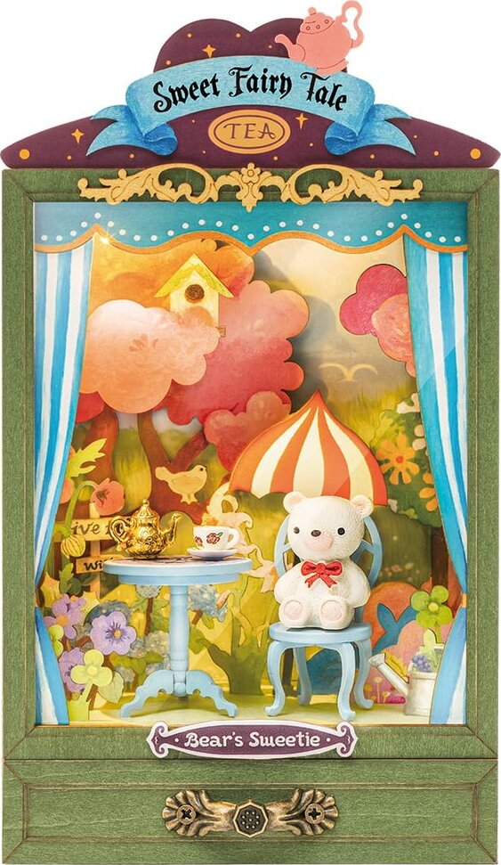 Bear's Sweetie DIY kit by Robotime features a charming scene with a white bear sitting on a blue chair at a table with a teapot and cup. The backdrop showcases a whimsical garden with colorful trees, flowers, and an umbrella, creating a delightful fairy tale atmosphere.