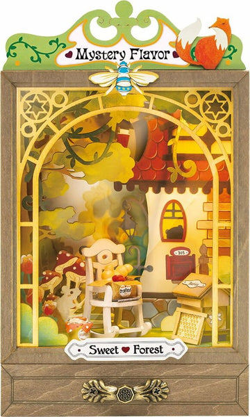 The Sweet Forest DIY kit by Robotime, featuring a charming miniature scene. This intricate design includes a wooden chair, a small table with crafted items, and a colorful landscape with trees and mushrooms. The backdrop has a whimsical house with a friendly fox and a bee motif on top, enhancing its enchanting appeal.