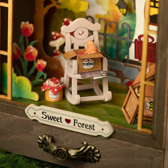 The Sweet Forest DIY kit by Robotime features a charming miniature scene with a white rocking chair, cute flower decorations, and tiny containers labeled 'crafted' and 'honey'. The kit allows users to create a delightful forest-themed display.