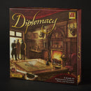 Cover of Diplomacy board game by Avalon Hill Hasbro, showcasing a richly decorated room with a fireplace, a map of Europe on a table, and three figures discussing strategies. The game emphasizes international intrigue, trust, and treachery.