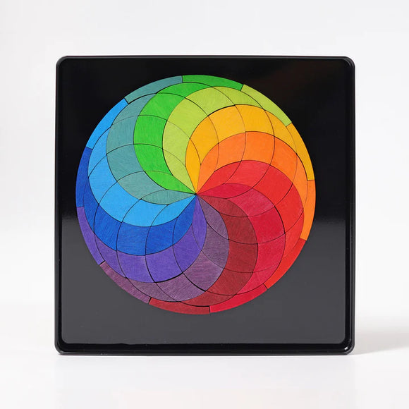 Magnet Puzzle Color Spiral by Grimm's featuring a vibrant, circular design composed of multi-colored wooden pieces arranged in a spiral pattern, set on a black background. Ideal for imaginative play and fine motor skills development.