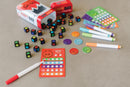 Fiesty Dice game by MindWare featuring colorful dice with expressive designs, scoring cards, and markers arranged on a light gray surface. The game includes base dice in various colors alongside scoring chips, creating a vibrant and engaging setup for players.