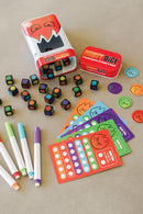 A vibrant display of Fiesty Dice game by MindWare, featuring colorful dice with cartoonish flame faces, scoring cards, and markers. The game is packaged in a playful tin and encourages creative gameplay with friends and family.