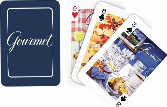 A set of Gourmet Poker Sized Playing Cards featuring artistic illustrations. The card back is a deep navy blue with the word 'Gourmet' elegantly written in white. Visible face cards include a red heart displaying drinks at a table, a black spade with a colorful fall leaf design, and another showing a still life of tableware and baked goods.