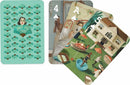 Set of Janet Hill Playing Cards by New York Puzzle Company, featuring colorful and artistic designs. The back of the cards shows a pattern of fans and the name 'JANET HILL STUDIO,' while the front displays various cards with unique artwork, including people in a garden and a house, showcasing vibrant and charming illustrations.