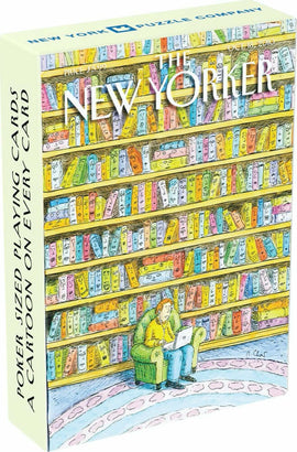 The Book Lover Playing Cards by New York Puzzle Company features a whimsical illustration of a person sitting in a green chair with a laptop, surrounded by colorful bookshelves filled with various books. Each playing card showcases a different cartoon, celebrating the joy of reading.