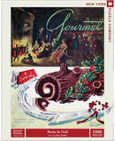 A 1000-piece jigsaw puzzle featuring a vintage illustration of a Buche de Noel on a delicate plate, surrounded by seasonal holly. The puzzle cover also displays scenes of festive gatherings and the title 'Gourmet: The Magazine of Good Living' at the top, with an artistic touch by Henry Stahlhut.