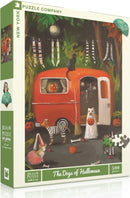 The Dogs of Halloween Puzzle by New York Puzzle Company features an illustration of festive dogs in costumes around a vintage red trailer, surrounded by pumpkins, Halloween decorations, and playful setting. The puzzle consists of 500 pieces and captures the whimsical spirit of Halloween.