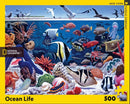 A vibrant jigsaw puzzle featuring an underwater scene filled with diverse marine life, including colorful fish, corals, jellyfish, and birds above the water's surface. The puzzle has 500 pieces and is created by New York Puzzle Company in collaboration with National Geographic.