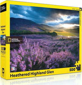 Heathered Highland Glen Puzzle by New York Puzzle Company, featuring a vibrant landscape of purple heather fields under a dramatic sky. The puzzle contains 500 pieces and is part of the National Geographic series.