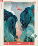 The Leap jigsaw puzzle from New York Puzzle Company features a whimsical illustration of a fox leaping through a vibrant forest. The artwork showcases lush, abstract trees in shades of blue and green, with hints of colorful accents, creating a dreamy landscape. The puzzle consists of 500 pieces and is made in the USA.