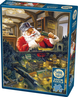 Santa's Railway jigsaw puzzle featuring a whimsical illustration of Santa Claus in a model train testing lab. The scene depicts a quaint town with illuminated houses, a vintage train passing through, and various details related to model trains. The puzzle box itself is colorful and includes the brand name Cobble Hill and details about the puzzle's size and a poster included.