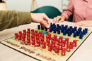 A close-up view of the Stratego game being played on a tabletop. A player is moving a red piece strategically on the board, which features intricate designs and a grid layout with blue and red pieces positioned in opposing formations.