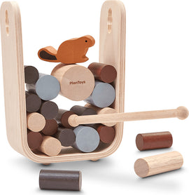 Timber Tumble game by Plan Toys featuring a wooden structure with colorful cylindrical blocks stacked inside. A beaver figure sits atop the stack, and a wooden mallet is included for play. The design promotes balance and dexterity for children.