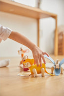 A child plays with a colorful DIY Triceratops toy from Plan Toys. The wooden dinosaur features a vibrant yellow body and small wooden limbs, engaged in imaginative play among other colorful animals. The warm, inviting environment suggests a playful atmosphere.