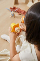 A child carefully assembles a colorful DIY Triceratops kit designed by Plan Toys. The kit features vibrant yellow, orange, and wooden elements, encouraging creativity and imaginative play.