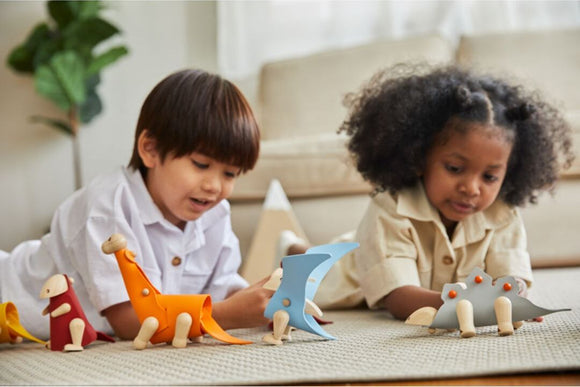 Two children playing on a carpet, assembling colorful Brachiosaurus DIY kits. They are focused on creating and enjoying the playful dinosaur figures made from wood and colorful materials.