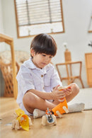 A young child sits on a wooden floor, focused on assembling the DIY Brachiosaurus kit from Plan Toys. The child is holding a piece of the kit while colorful dinosaur parts are spread out in front of them, showcasing an engaging playtime activity designed to foster creativity and fine motor skills.