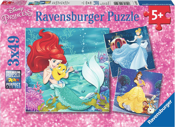 Princesses Adventure jigsaw puzzle by Ravensburger featuring three scenes of Disney princesses: Ariel from The Little Mermaid with Flounder, Cinderella in her ball gown near a castle, and Belle in her yellow dress with enchanted objects. The puzzle is colorful and suitable for children aged 5 and up.
