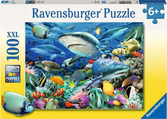 Ravensburger Shark Reef jigsaw puzzle featuring a vibrant underwater scene with multiple sharks, colorful fish, coral, and marine life. The puzzle contains 100 pieces and is designed for ages 6 and up, showcasing intricate details and bright colors in a premium quality format.