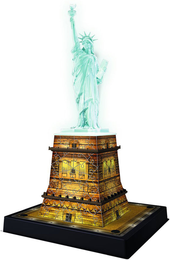 A detailed jigsaw puzzle featuring the Statue of Liberty illuminated at night, crafted by Ravensburger. The puzzle shows the statue atop a glowing pedestal, showcasing intricate designs and vibrant colors that capture the beauty of the iconic landmark.