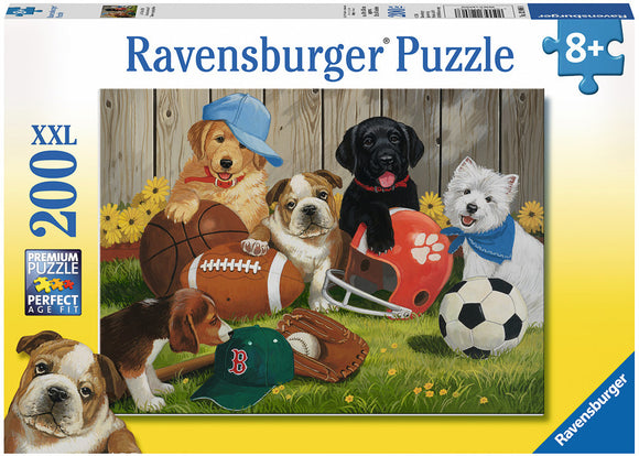 A colorful jigsaw puzzle box featuring a playful scene with five adorable puppies. The puppies are interacting with various sports equipment, including a football, baseball glove, soccer ball, and helmets. The background shows a wooden fence and flowers, creating a cheerful outdoor atmosphere. The puzzle is labeled as a Ravensburger product, designed for ages 8 and up, with 200 XXL pieces for easier handling.