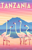 A vibrant jigsaw puzzle titled 'Tanzania' by Ravensburger. The artwork features five pink flamingos standing along a shoreline, with a picturesque backdrop of a mountain against a colorful sunset sky. The puzzle promises hours of engaging fun with its charming illustration.