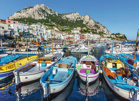 A vibrant jigsaw puzzle titled 'Colorful Marina' by Ravensburger. The image features a picturesque scene of a marina with colorful boats docked, set against a backdrop of charming coastal buildings and a striking mountainous landscape under a clear blue sky.