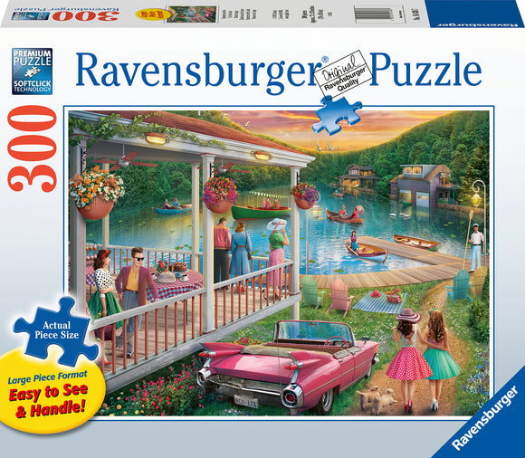 Ravensburger jigsaw puzzle titled 'Summer at the Lake' featuring a vibrant scene of people enjoying a lakeside setting with colorful flowers, boats, and a classic car. The puzzle has 300 pieces, large piece format for easy handling, and showcases a relaxed summer atmosphere.