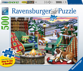 Ravensburger's Après All Day jigsaw puzzle featuring a cozy winter scene. The image shows a warm cabin porch with green adirondack chairs, a stone fire pit surrounded by snacks, two dogs resting on a mat, and a snowy landscape with trees and mountains in the background.