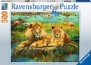A beautifully illustrated jigsaw puzzle featuring a family of lions – a majestic adult lion and lioness, along with a playful cub – sitting together by a serene water body. The background showcases a vibrant savanna landscape with colorful flamingos and lush greenery, making it a captivating scene for puzzle enthusiasts.