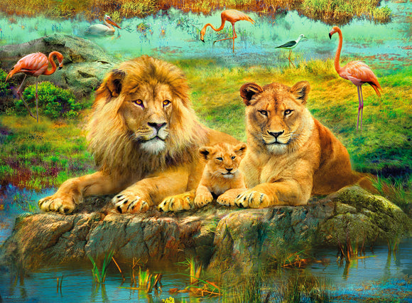 A beautiful jigsaw puzzle featuring a family of lions lounging on a rock near a serene body of water. The majestic male lion, a lioness, and their playful cub are surrounded by a lush savanna landscape with colorful flamingos and other wildlife in the background. The vibrant colors and detailed artwork create a captivating scene perfect for puzzle enthusiasts.