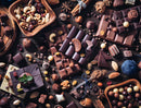 A beautifully arranged flat lay of assorted chocolates and nuts. The image features various types of chocolate bars, chocolate-covered nuts, and decorative elements like mint leaves and wooden bowls filled with mixed nuts. The rich brown tones contrast against the wooden background, creating a mouthwatering visual appeal reminiscent of a dessert paradise.