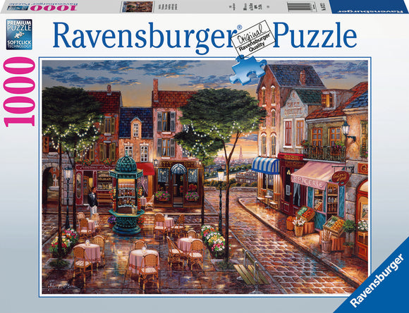 A Ravensburger jigsaw puzzle titled 'Cafe Scene' featuring a charming street lined with cafes, shops, and tables under twinkling lights. The setting captures a vibrant evening atmosphere with intricate details, inviting viewers to piece together a picturesque outdoor scene reminiscent of a cozy European cafe.