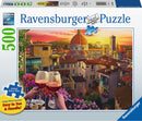 A Ravensburger 500-piece jigsaw puzzle titled 'Cozy Wine Terrace', featuring a scenic view of a city at sunset, with two glasses of red wine in the foreground. The puzzle box includes details about premium quality and large piece format, making it visually appealing and easy to handle.