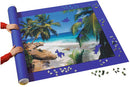 The Giant Puzzle Stow & Go! by Ravensburger is a jigsaw puzzle in progress, featuring a vibrant beach scene with palm trees and blue ocean. A person is rolling up the puzzle on a mat designed to keep pieces secure, while scattered puzzle pieces are visible around the edges.