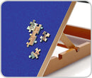 Close-up view of a wooden jigsaw puzzle board featuring several puzzle pieces placed on a blue felt surface. The sturdy wooden frame holds the pieces in place, ideal for puzzle enthusiasts.
