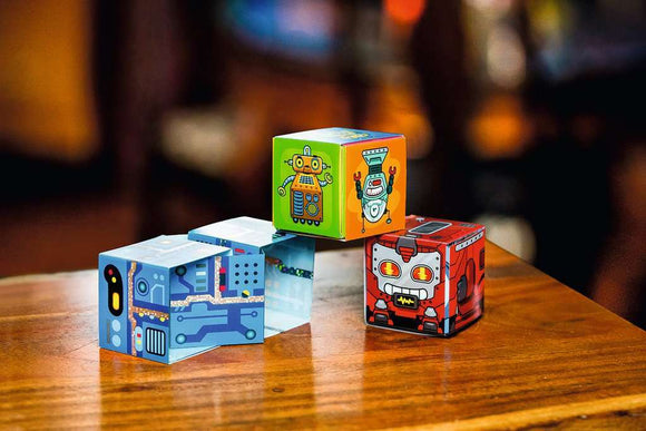 A vibrant display of Block Chain Robots by Thinkfun, featuring three colorful mechanical puzzle cubes with cartoon robot designs. The cubes are arranged playfully on a wooden surface, showcasing intricate patterns and bright colors that engage the imagination.