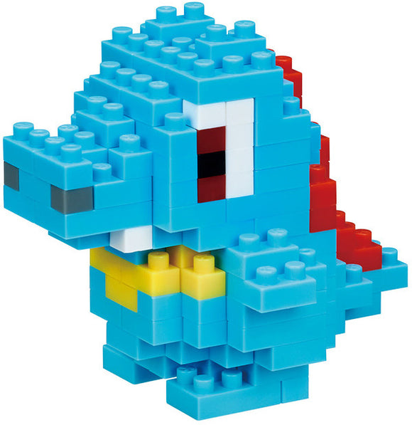 Nanoblock Totodile DIY kit from Schylling Associates Inc. The assembled figure is a small, pixelated dinosaur made of colorful blocks in blue, red, white, and yellow.