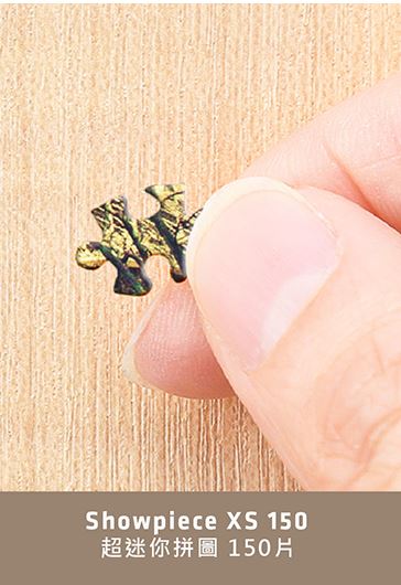 A close-up image of a hand holding a single jigsaw puzzle piece. The piece is intricately designed with a colorful pattern that includes shades of green and gold. This image represents the Puppies in a Gift Box XS 150 pc Puzzle by Pintoo, showcasing the quality and detail of its pieces.