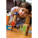 A young child engrossed in play with Castle Logix by SmartGames, carefully manipulating colorful wooden blocks featuring castle-related designs on a wooden floor, fostering creativity and problem-solving skills.